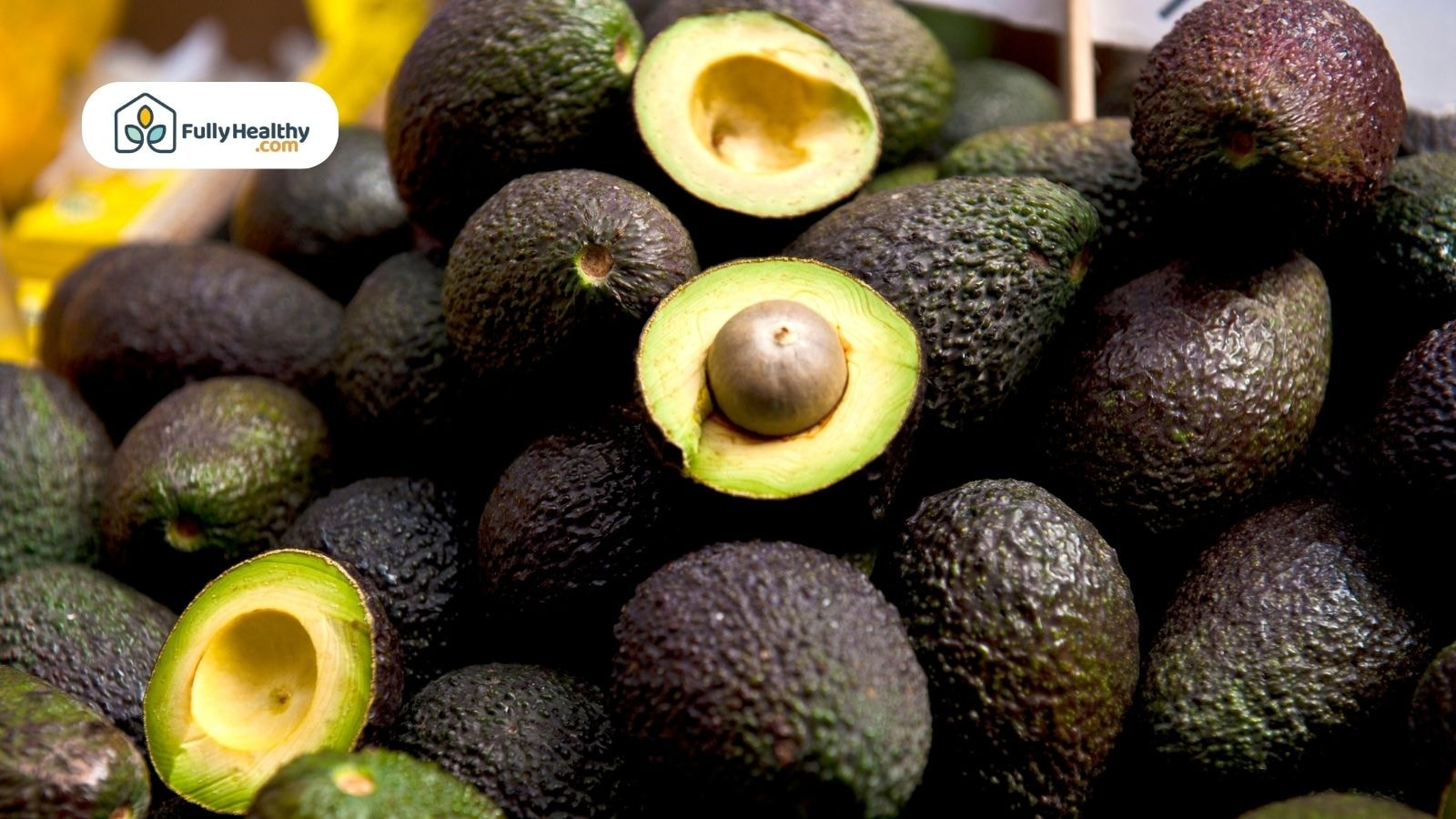 Dark hass avocados with cut halves showing yellow green ripe flesh