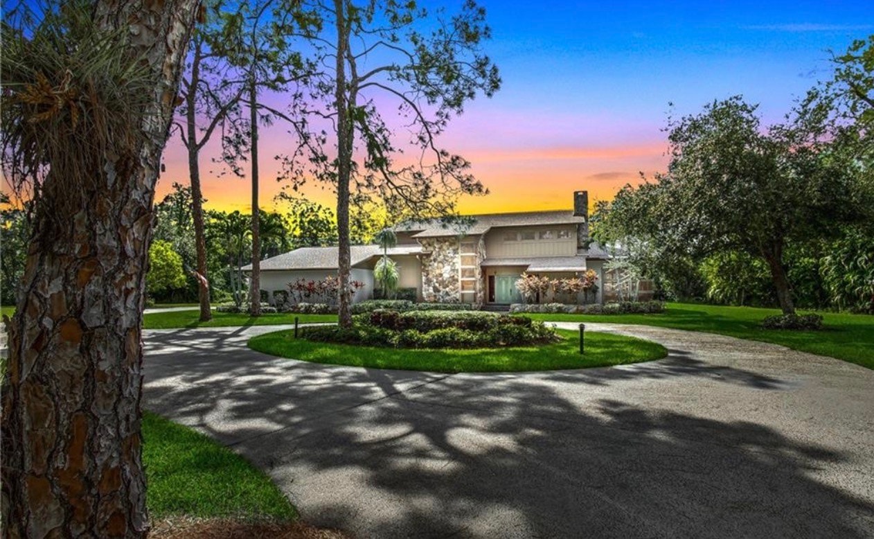 The image depicts a luxurious home exterior surrounded by mature oak trees and private landscaping, providing a serene and secluded atmosphere. This elegant property is located in the Brynwood neighborhood of Fort Myers, showcasing the charm of Brynwood real estate.