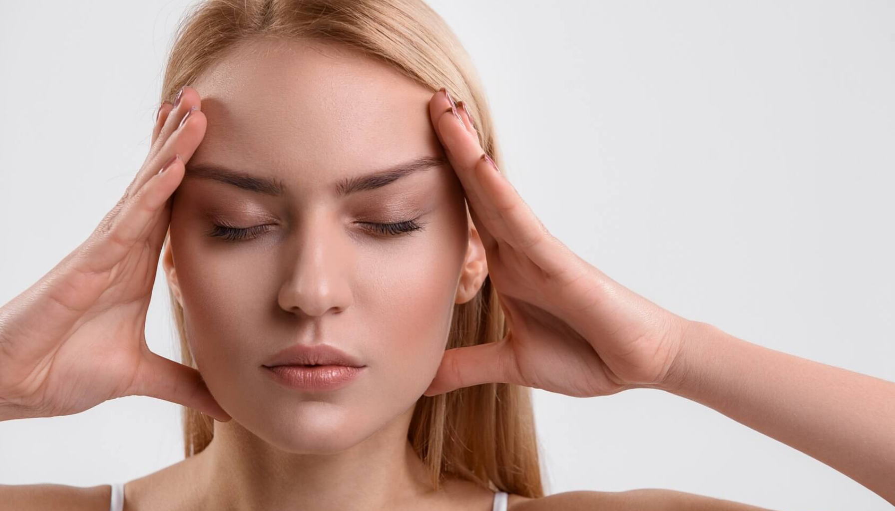 "Kvinne med lukkede øyne holder hodet med begge hender, ser ut til å oppleve stress eller hodepine."