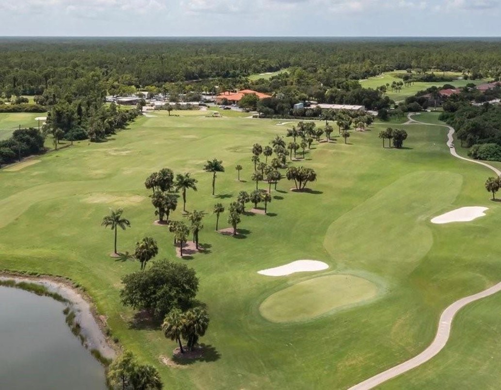 The image depicts the entrance gate to the Valencia Country Club, featuring a guard house and beautifully manicured landscaping that highlights the welcoming atmosphere of this premier gated community. This scene represents the vibrant and relaxing environment of the Valencia Country Club in Naples, known for its luxurious amenities and stunning golf course views.