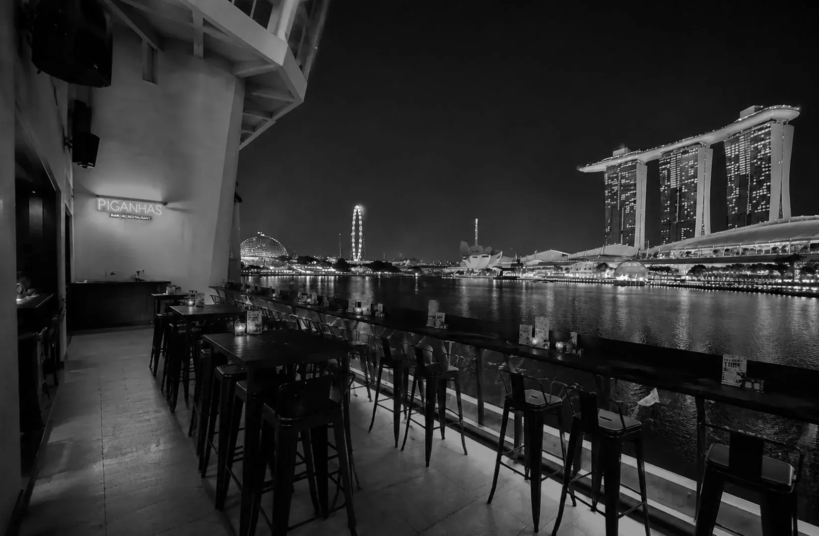 Outdoor dining area at Kinki Restaurant + Bar overlooking Marina Bay and the Singapore skyline at night.