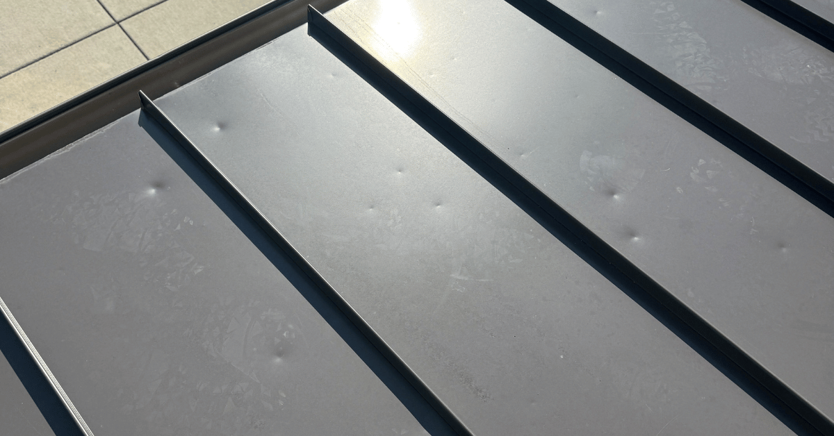 Dents visible on a standing seam metal roof caused by hail, underscoring the importance of regular roof inspections after storms.