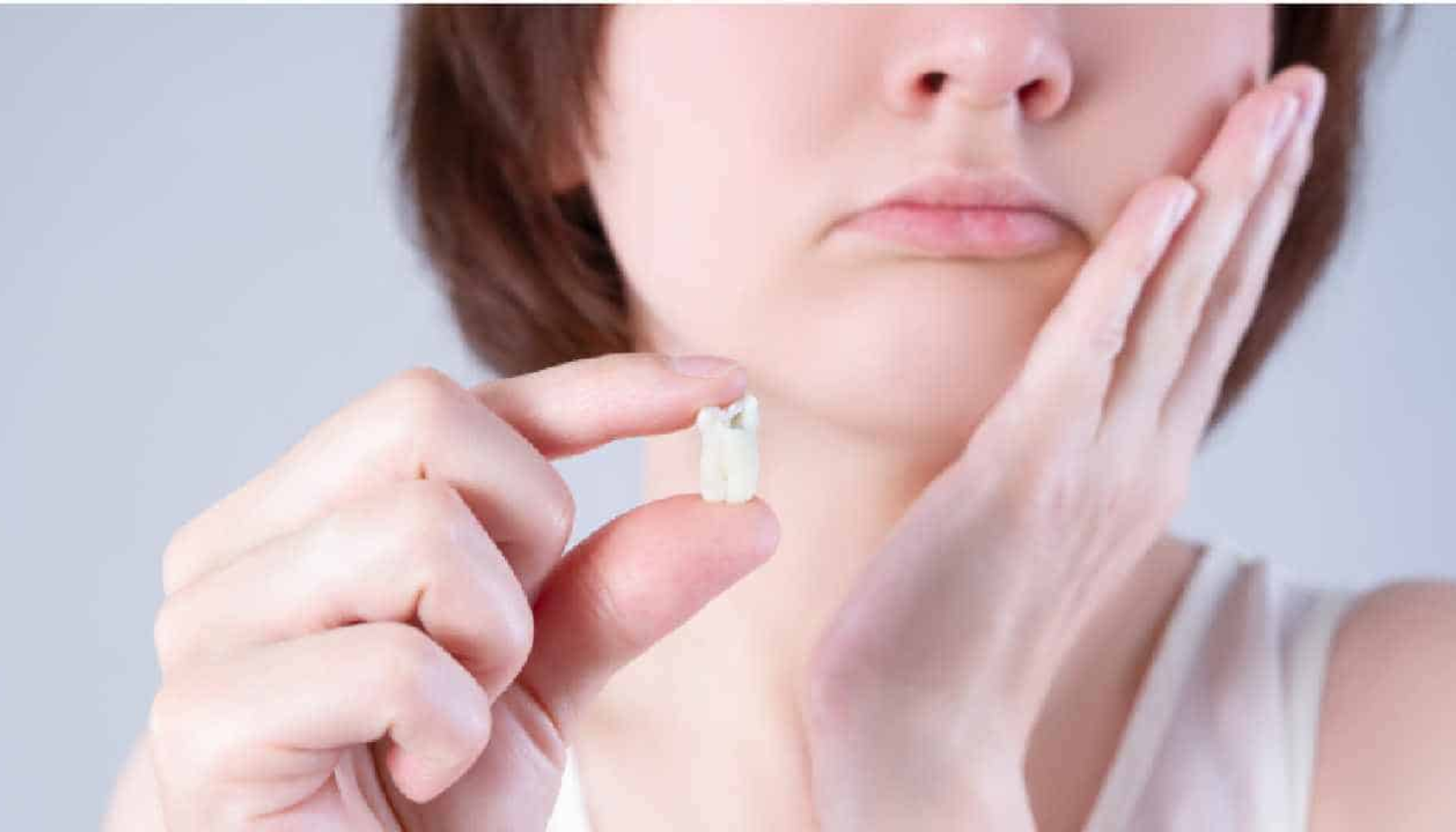 Person med smertefullt uttrykk holder en trukket tann i hånden og tar seg til kinnet etter tanntrekking.