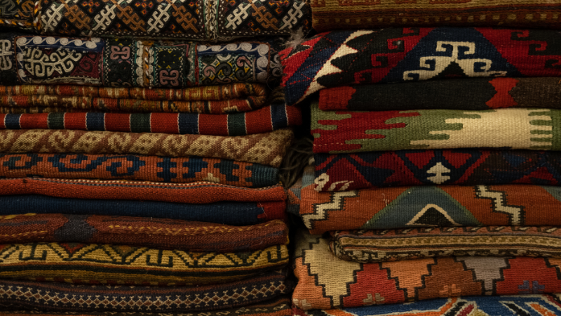 A pile of different colored and patterned woven and knitted rugs.