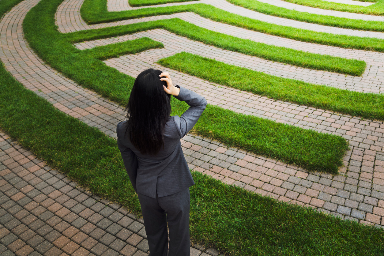 A woman in a suit looking at a winding maze symbolizing uncertainty in her career path.