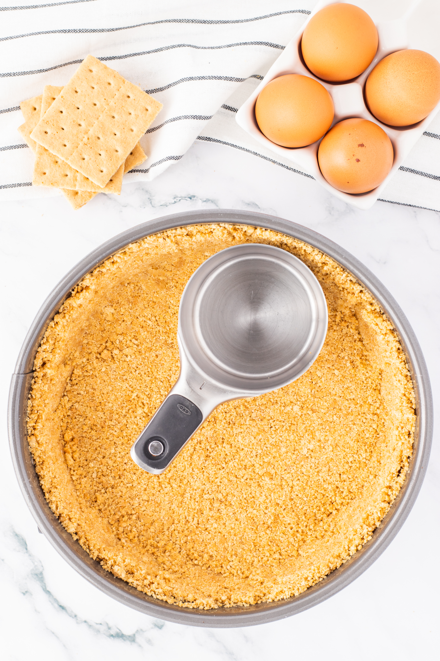 graham cracker crust pressed into springform pan with a measuring cup
