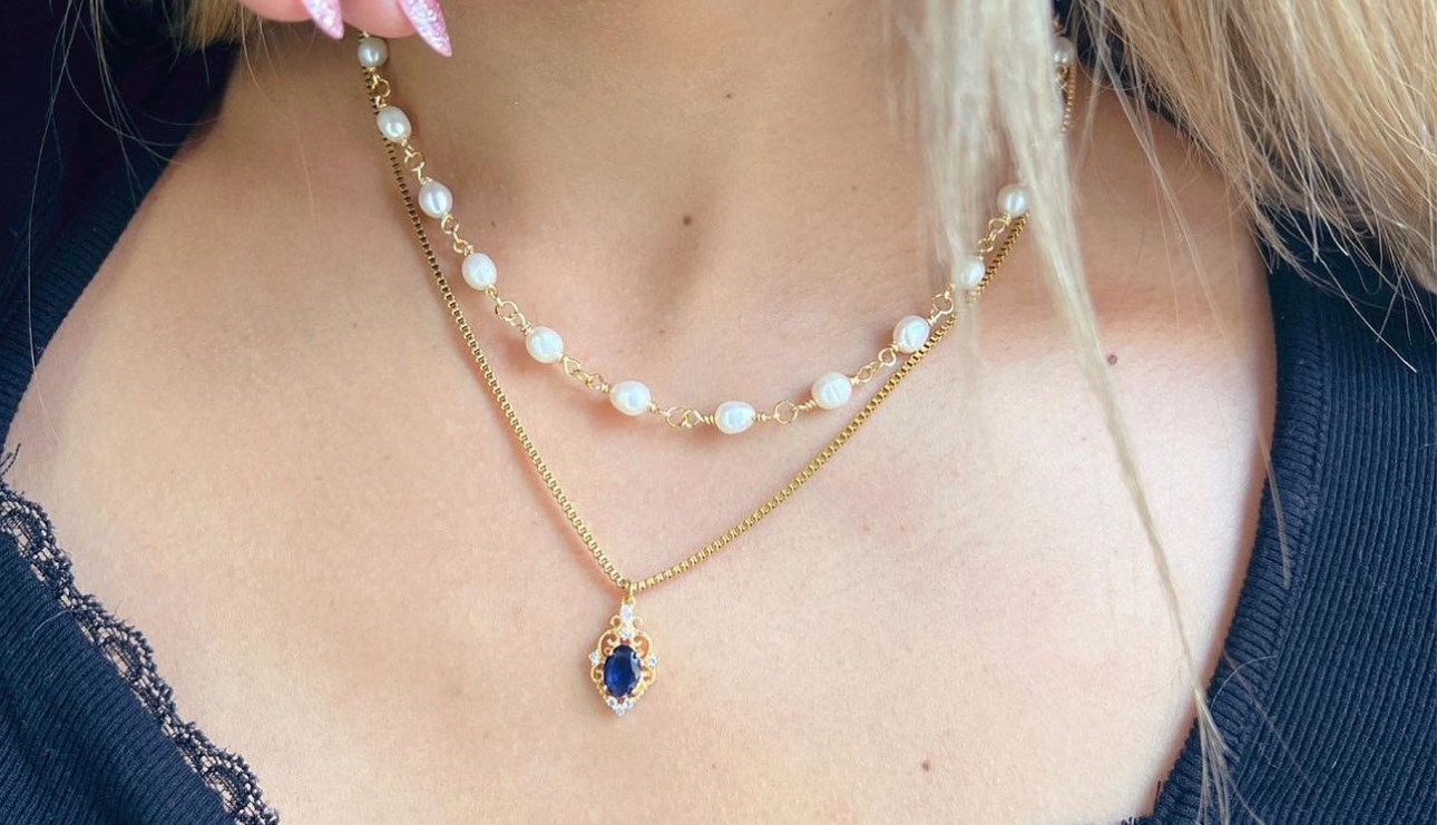 Close-up of a woman's neck adorned with two necklaces, one with pearls and the other featuring a blue zircon pendant, illustrating the variety and elegance of hypoallergenic jewelry.