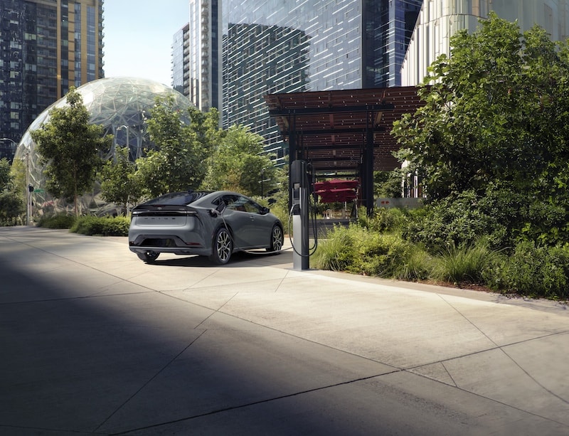A Toyota Prius Plug-in Hybrid charging in a futuristic city setting, demonstrating its eco-friendly efficiency and innovation at AutoFair Toyota of Tewksbury in Tewksbury, MA.