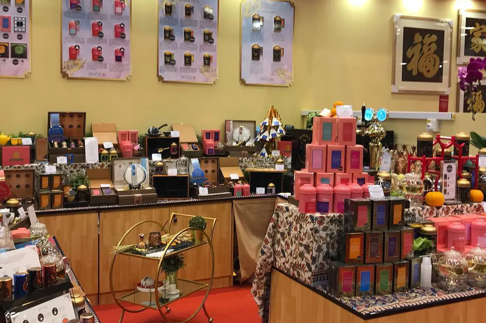 Retail store display showcasing stacked tea tins, gift boxes, product wall posters, framed calligraphy, and a gold serving cart.