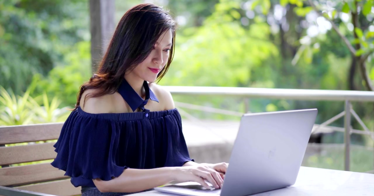 A focused woman working outdoors on her laptop, reviewing details about the 1099 tax percentage.