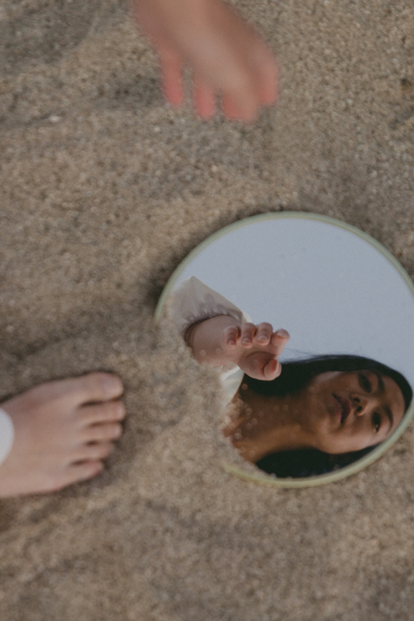 a woman looks at her reflection in a mirror in the sand