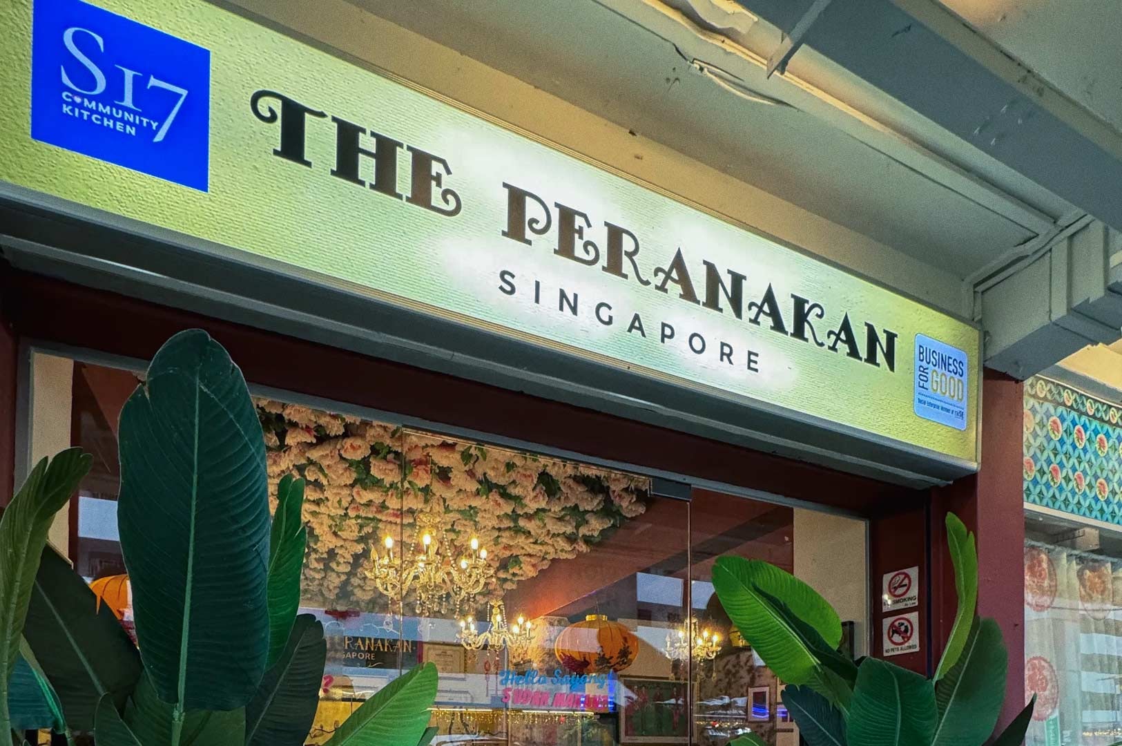 The Peranakan Singapore restaurant entrance with decorative plants and signage.”