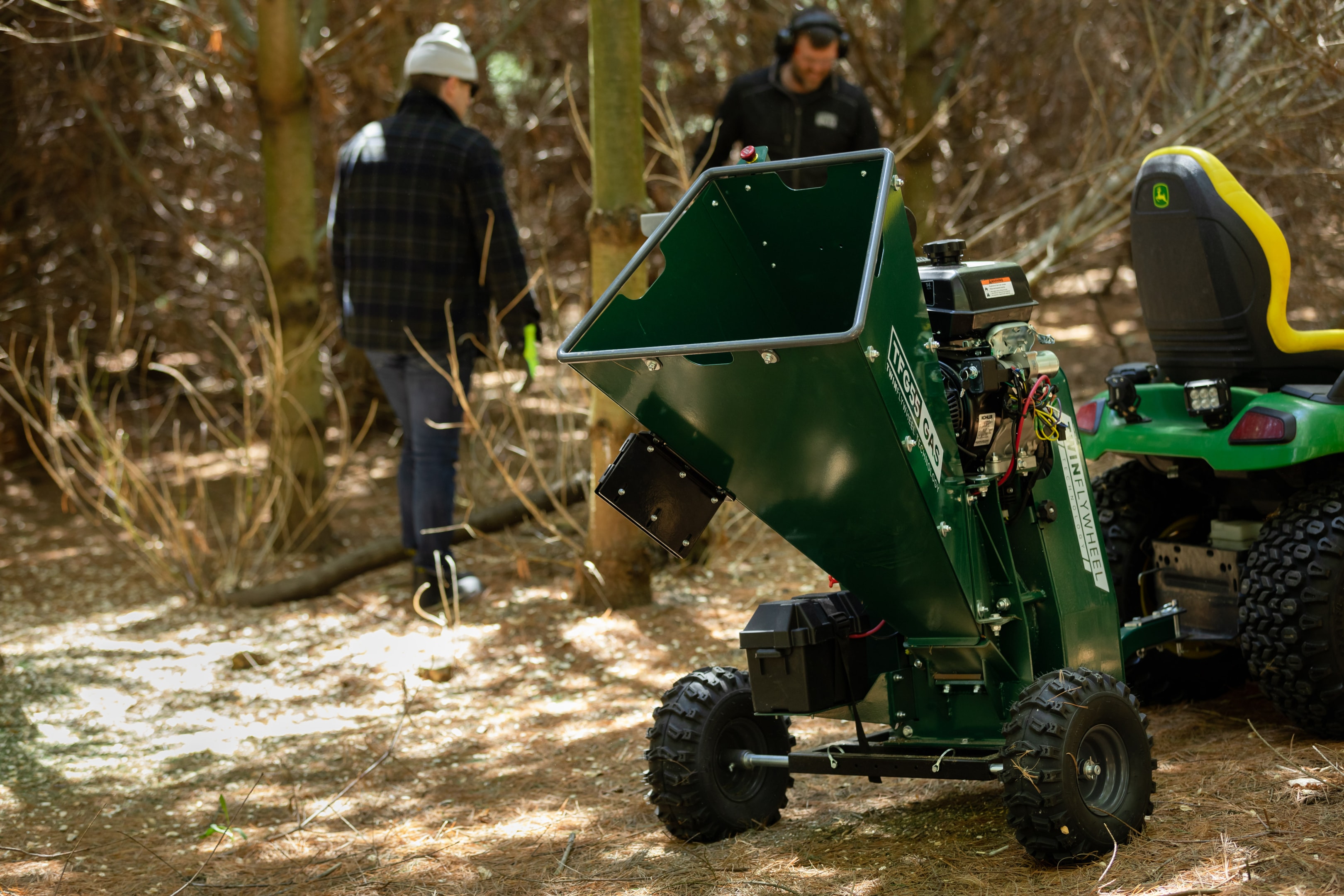 A TFG55 PTO Wood Chipper sitting on a subcompact tractor in a woodlot.