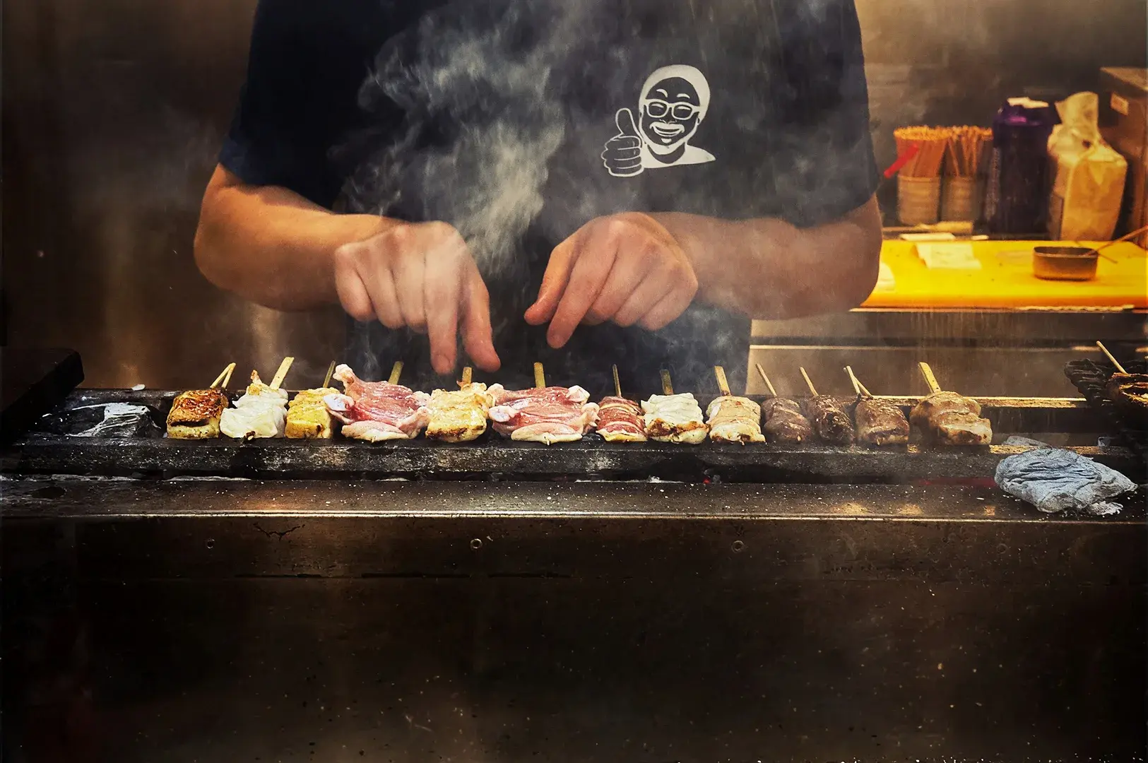 Chef grilling assorted yakitori skewers over a charcoal fire at Sakedoro Eizaburo in Fortune Centre, showcasing the open-kitchen atmosphere.