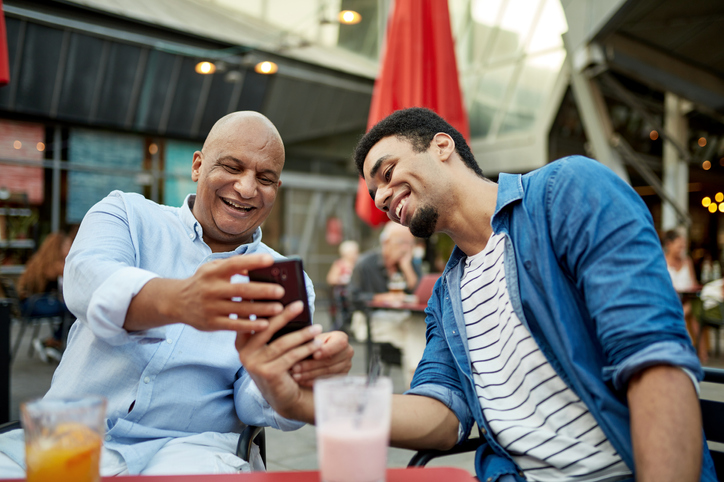 Dad and adult son sitting outside enjoying smoothies. 