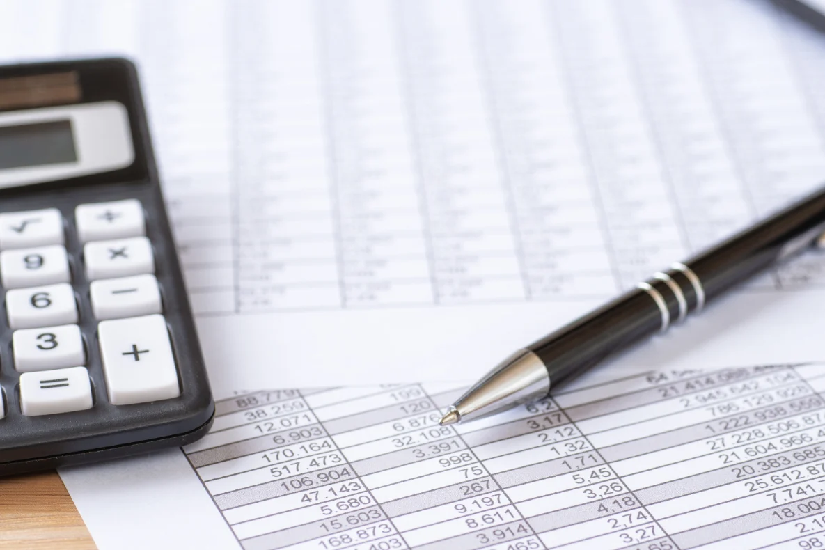 A calculator and a pen rest on a document filled with numbers and lines.