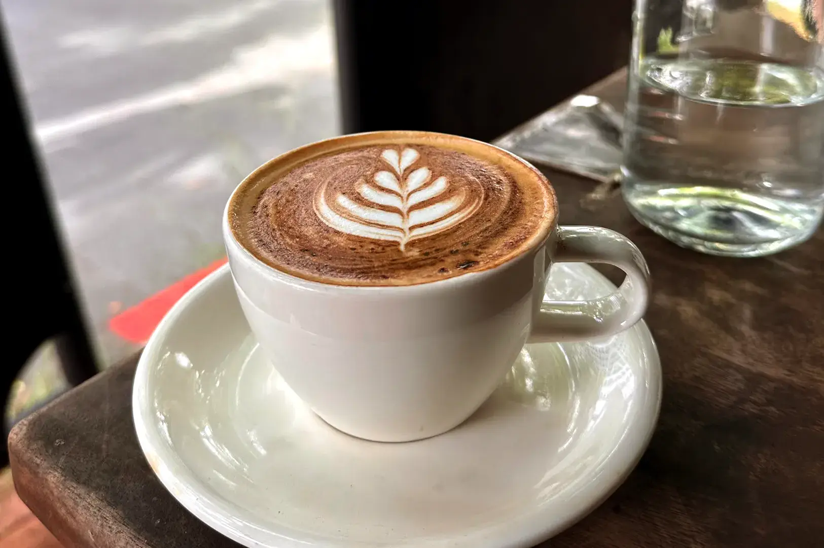 A freshly brewed cup of specialty coffee with intricate latte art on a wooden cafe table.