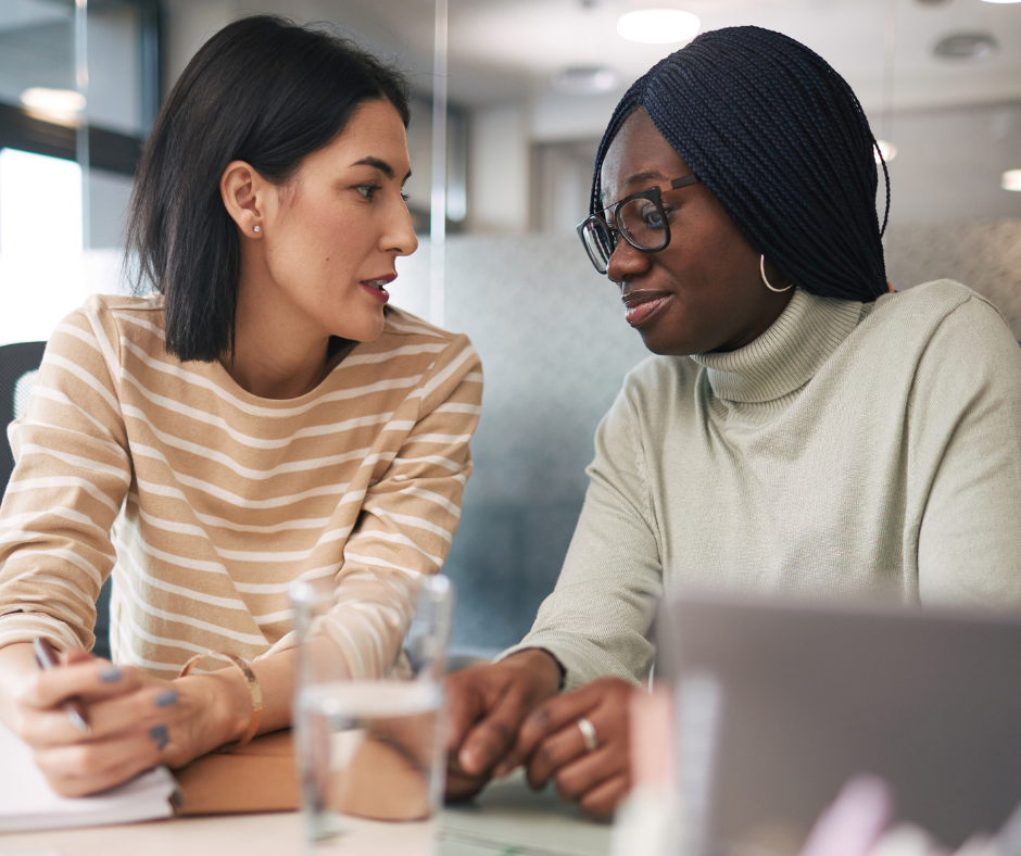 two women sit together at a desk talking