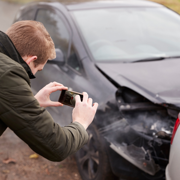 A photograph showing someone taking pictures of a car accident scene.