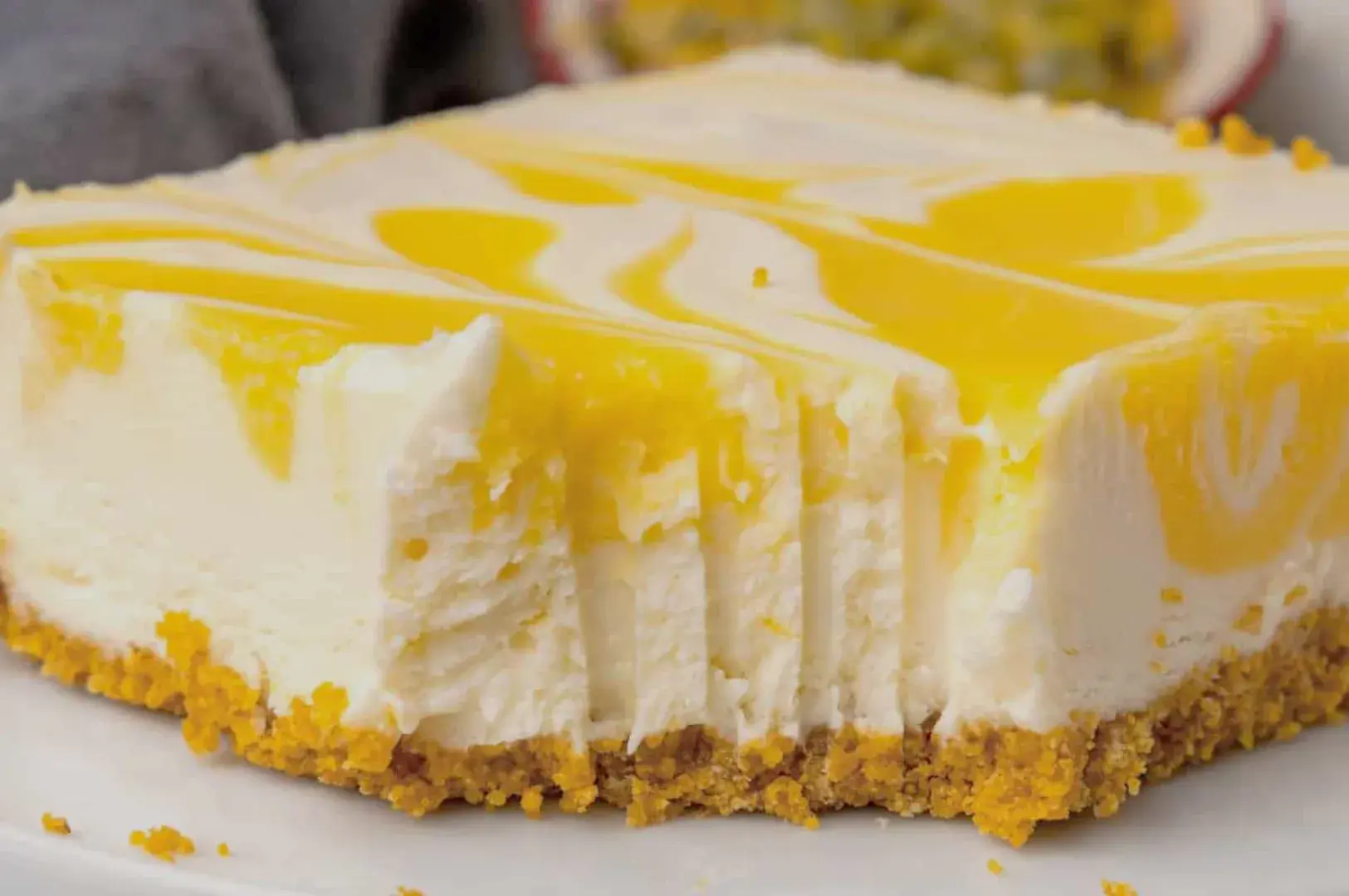 A slice of cheesecake with a yellow swirl on top, resting on a graham cracker crust.