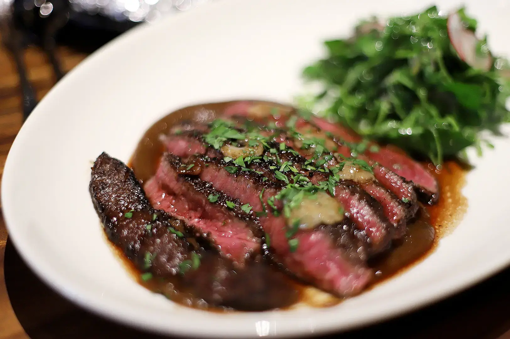 Singapore steakhouse sliced medium-rare steak with mushroom sauce, herbs and leafy greens