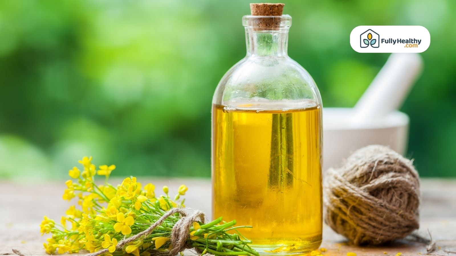 Glass bottle of canola oil beside yellow flowers and twine