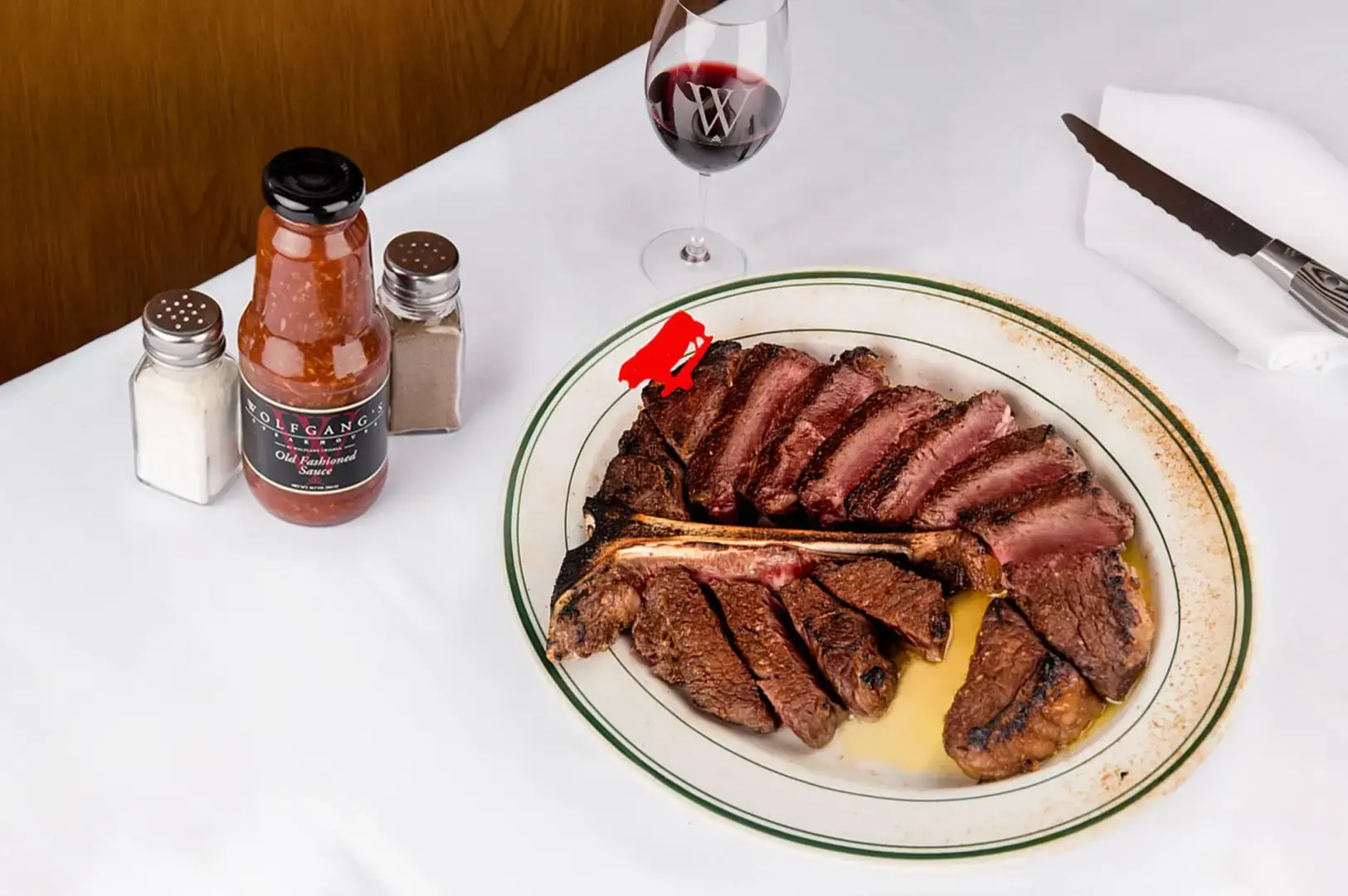 Wolfgang's Steakhouse platter with sliced steaks, bone-in beef, wine and classic steakhouse sides