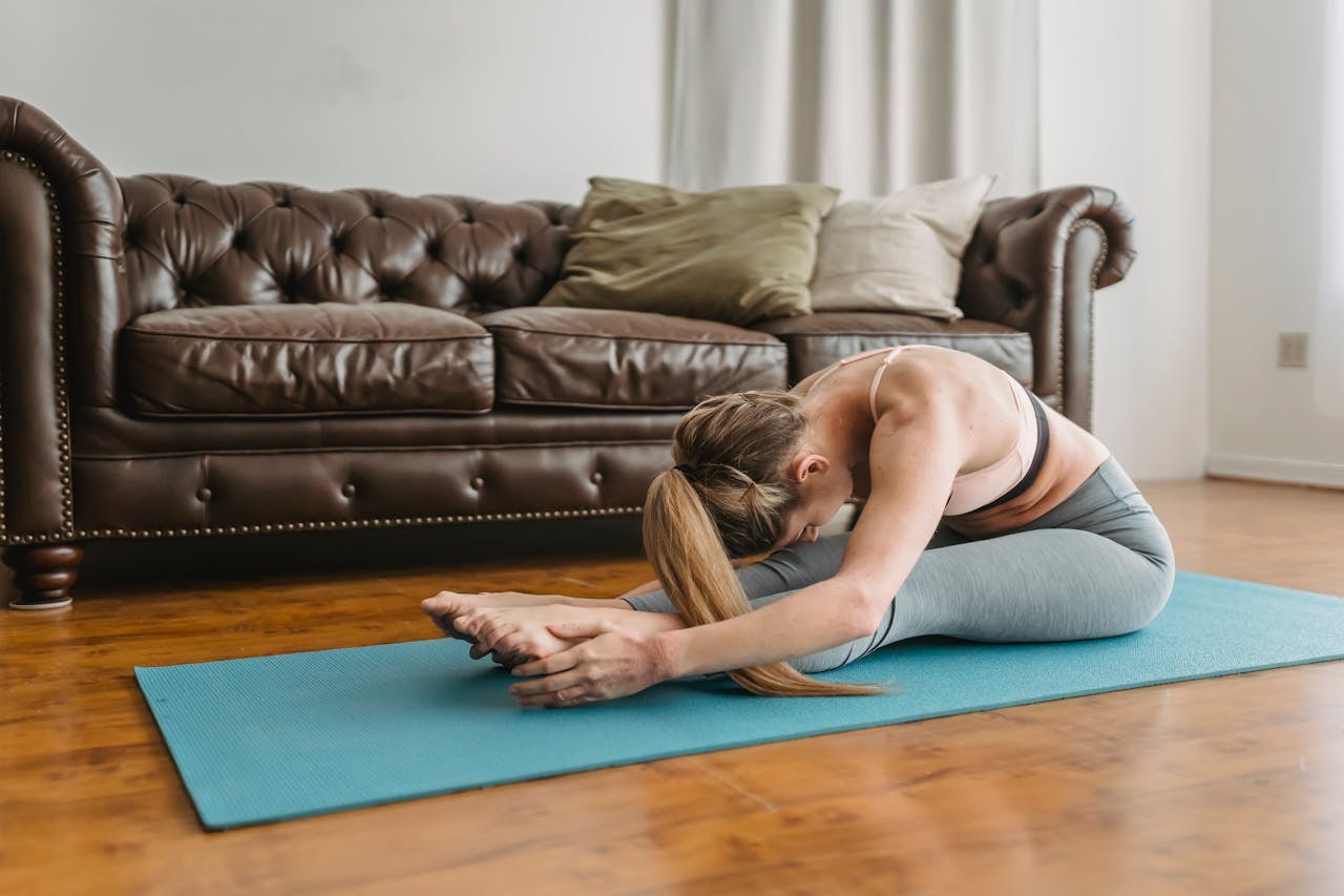 Stretching exercises for the spine as a woman folds forward in a seated stretch on a yoga mat at home.