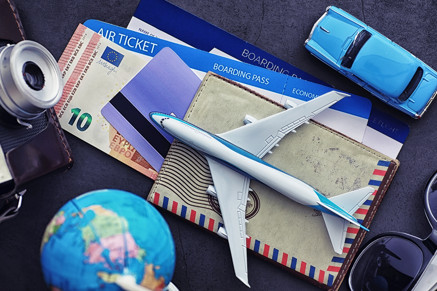 a toy plane, passport , globe, sunglasses, camera, a blue toy car, boarding pass, flight ticket