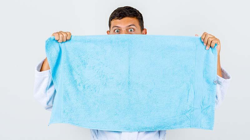 A man with a blue microfiber towel in front of his face