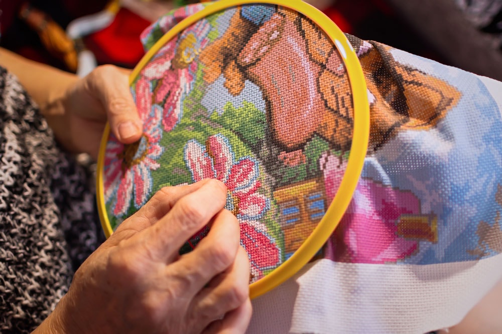 An elderly woman holds a hoop and thread with a needle in her hands. Soft focus. The concept of hobby and manual labor.