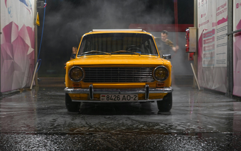 Yellow classic car being washed at a self-service car wash with water spray and steam