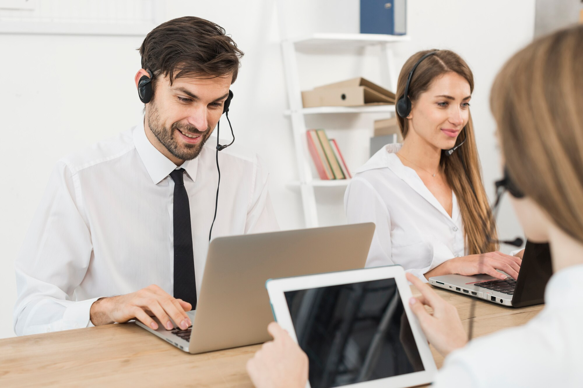 Three people sit at a table in front of tablets and ipads, all using headsets like in a Voip Contact Center