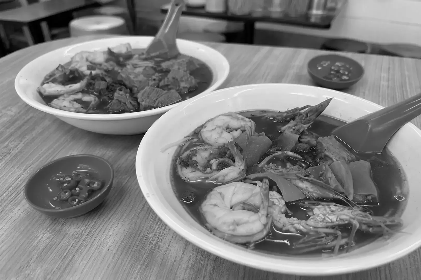 Two bowls of prawn noodle soup served with sliced chili on the side.