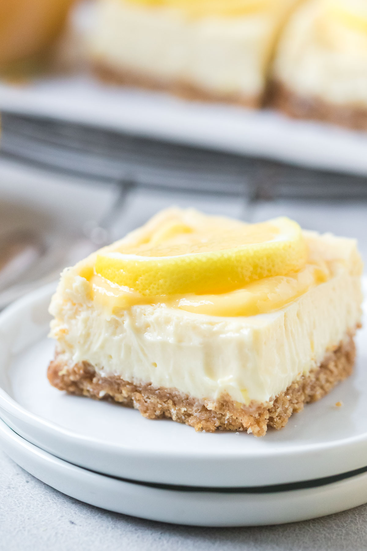 lemon cheesecake bar topped with lemon slice sitting on two small white plates
