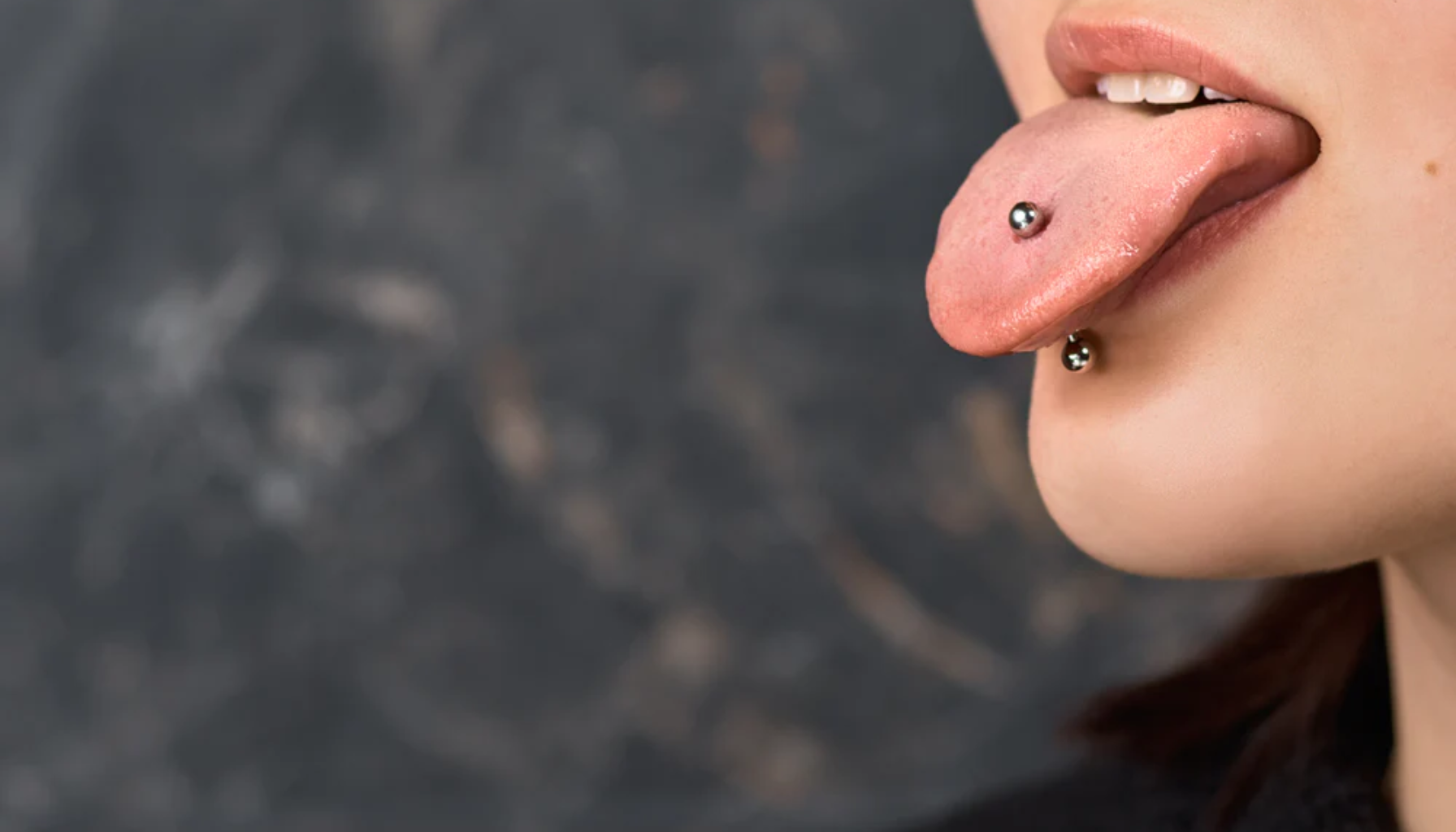 Person med både tunge- og leppepiercing som stikker ut tungen.