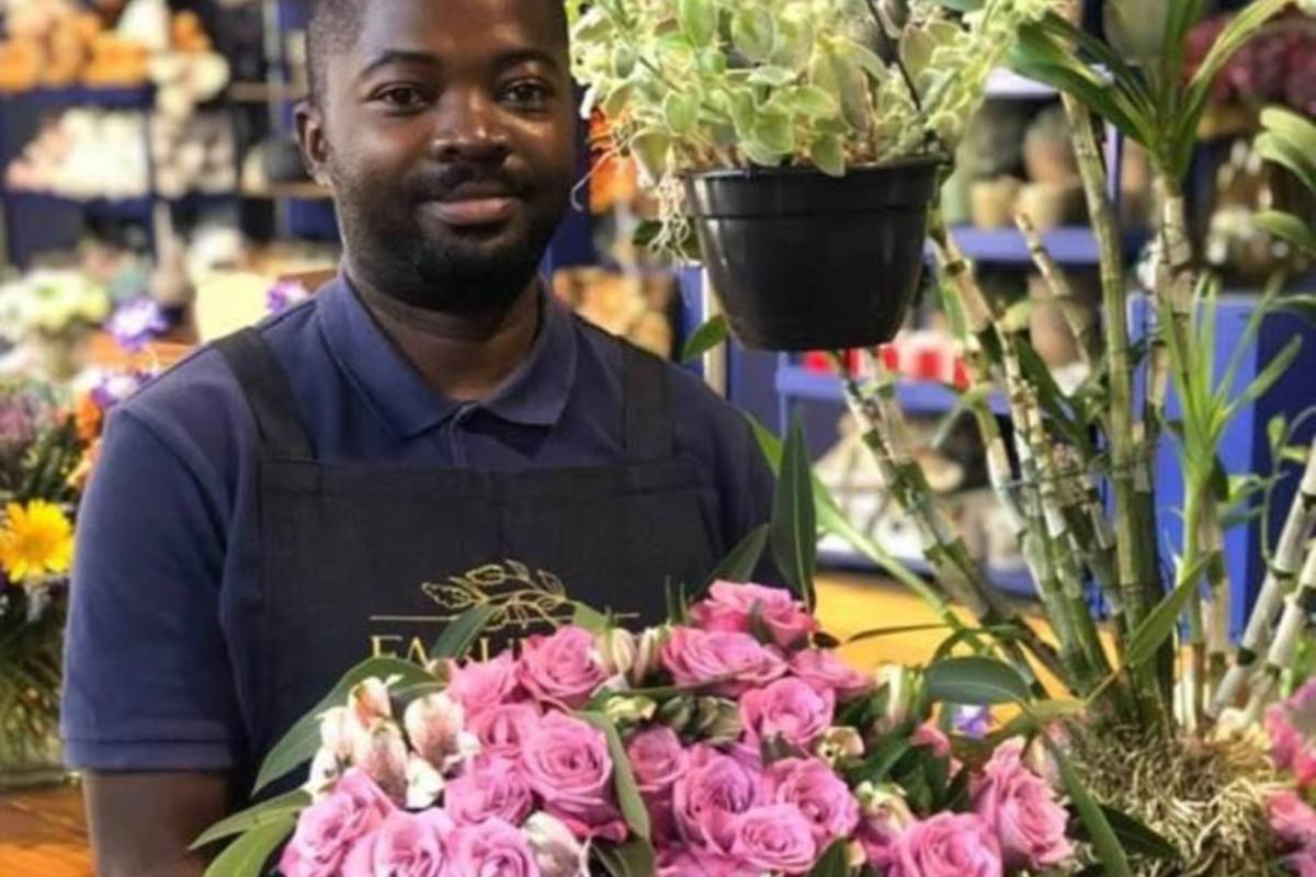 Black man holding a flower arrangement and smiling, pink flowers, about to deliver flowers