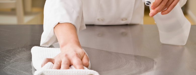 A chef wiping a stainless steel prep table showing food grade sanitisers are used in the kitchen to clean surfaces