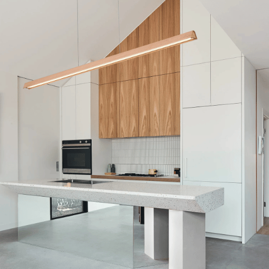 Minimalist kitchen with white cabinetry, wooden accents, a terrazzo island, and a sleek linear pendant light hanging above the countertop.