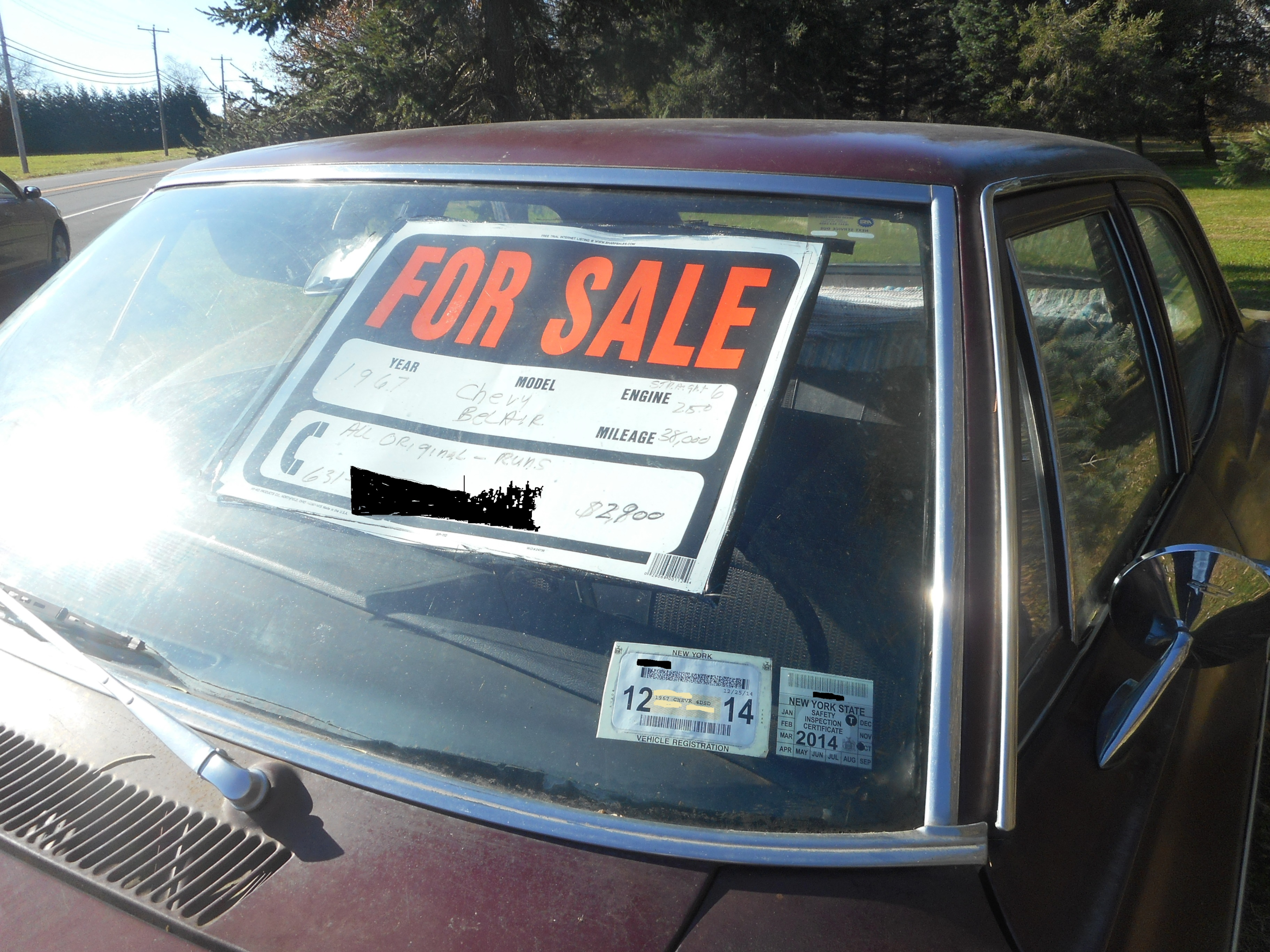 A car parked in front of a house with a "For Sale" sign on it