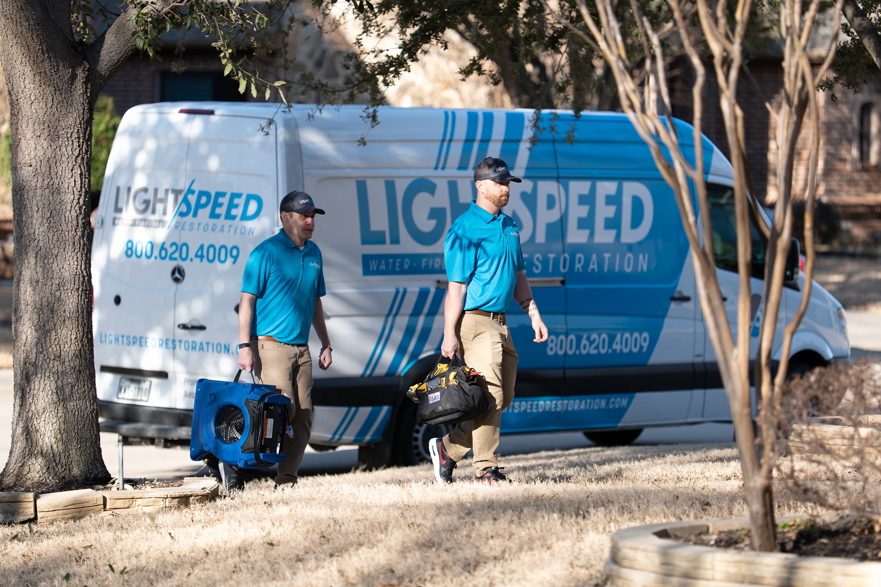 A professional water damage restoration crew is unloading advanced equipment from a service truck at a residential property, ready to begin the emergency water extraction and restoration process. The technicians are equipped to handle water damage emergencies, aiming to minimize damage and prevent mold growth for homeowners in Austin, TX.