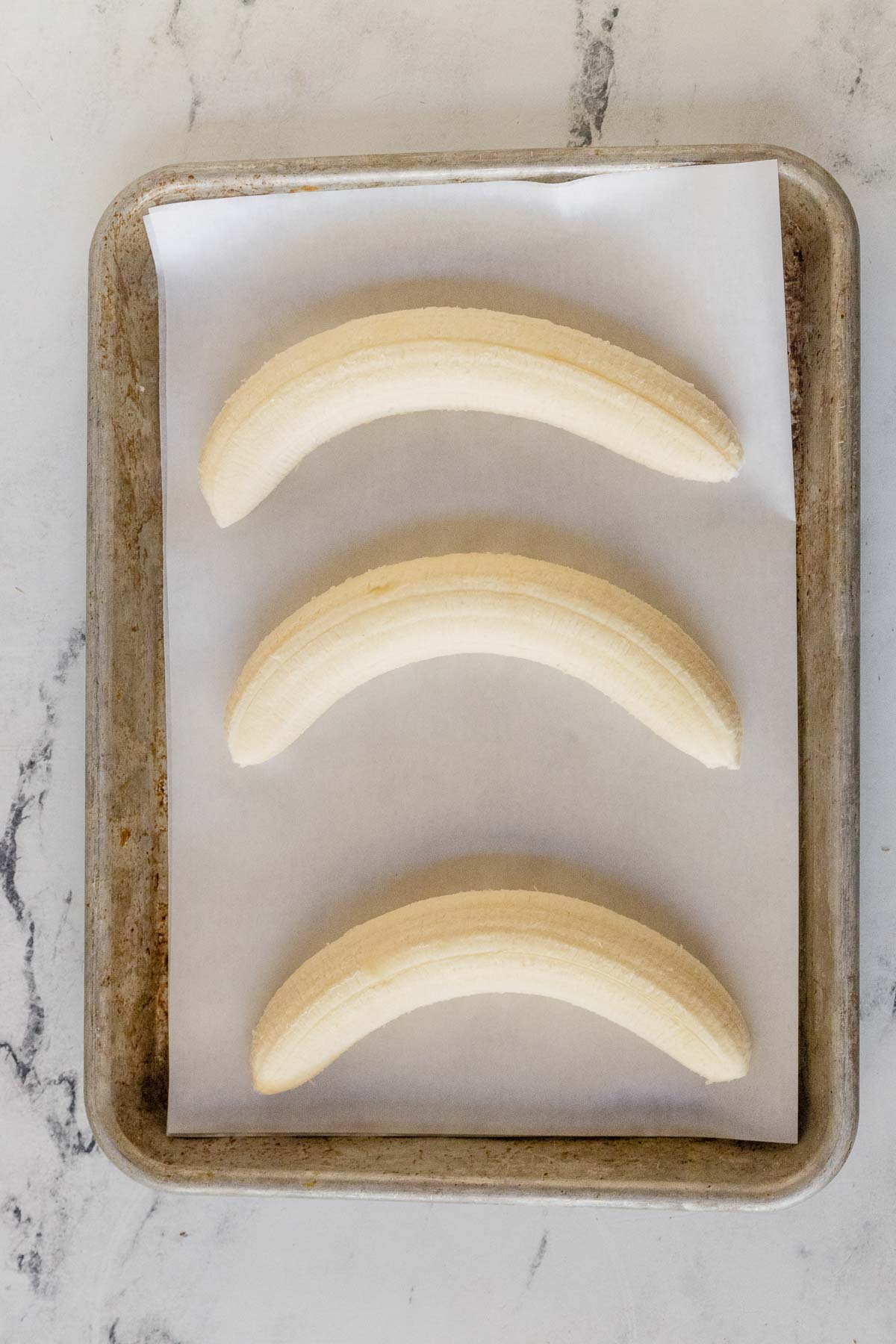3 peeled bananas on a baking sheet with parchment paper