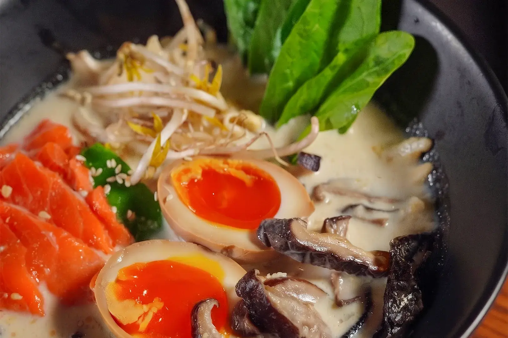 Bowl of creamy ramen topped with fresh salmon, marinated soft-boiled egg, shiitake mushrooms, and bean sprouts.