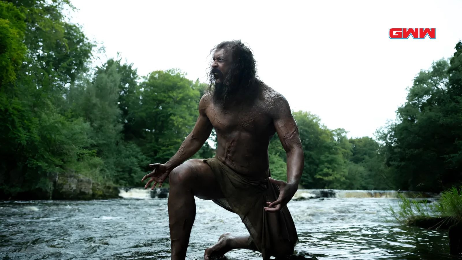Chi Lewis-Parry as Samson kneeling shirtless and roaring in river scene