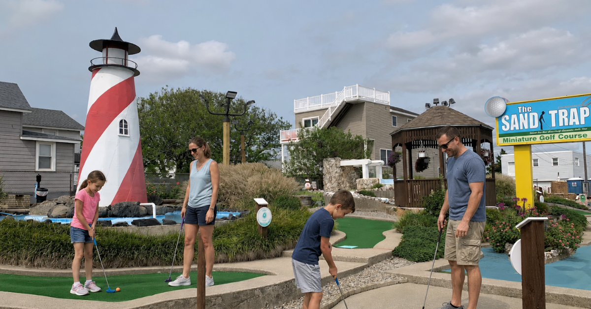 Family playing mini golf at The Sand Trap course in Ship Bottom, NJ with historic lighthouse nearby, featuring popular Jersey Shore family activities and entertainment