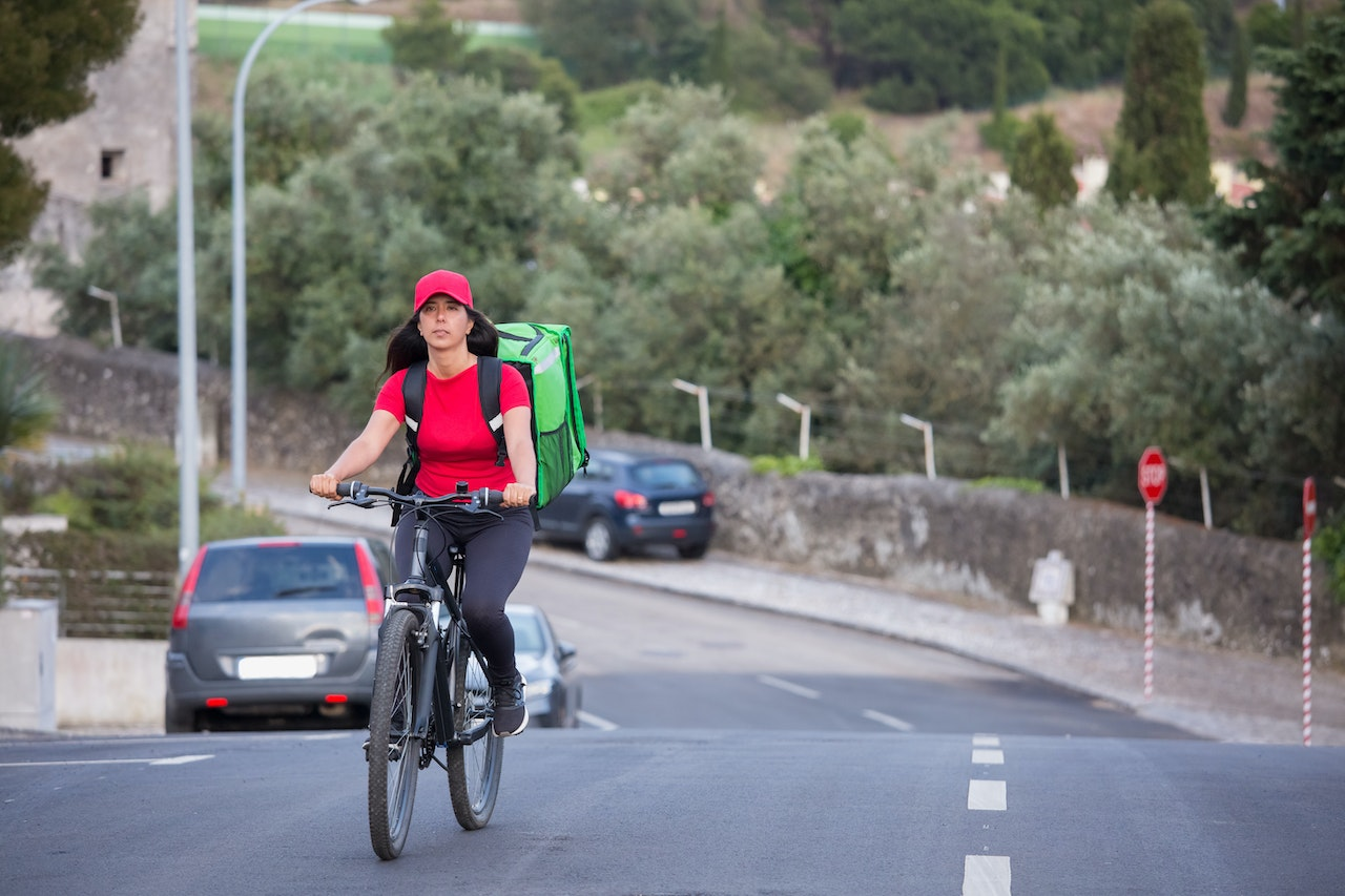 Entregador de bike pedalando no trânsito. Foto: Pexels