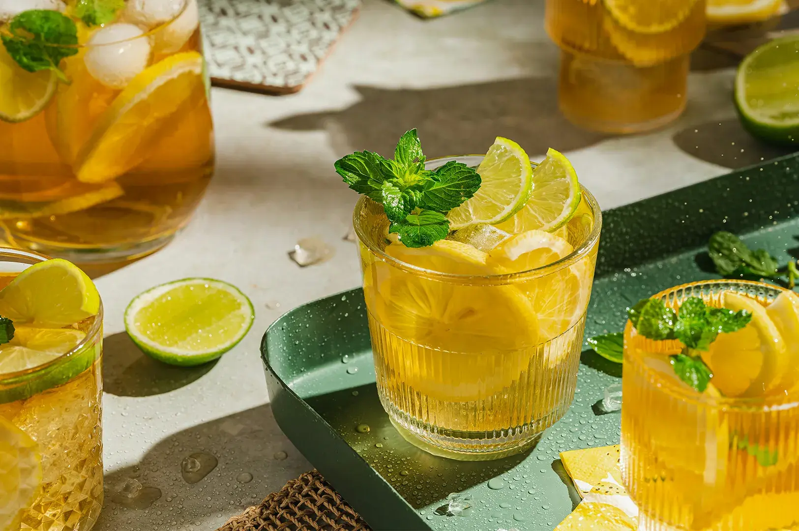 Glasses of iced lemon tea with mint sprigs on a green tray.