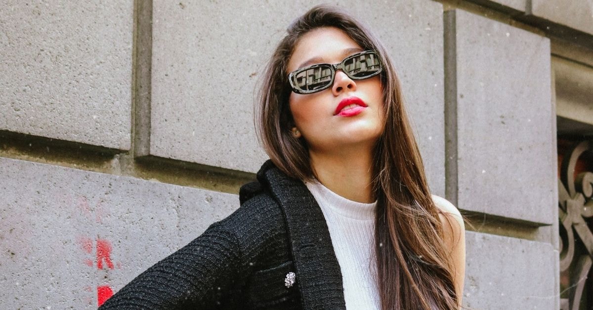 Fashionable woman with sunglasses poses against a wall, showcasing her style amid the surcharge news.