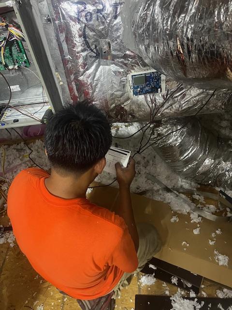 The image depicts a Trane furnace installation in an attic, showcasing proper venting and connections for an efficient HVAC system. A navy-shirted technician is seen working on the installation, emphasizing the importance of professional HVAC installation for optimal energy efficiency and performance.