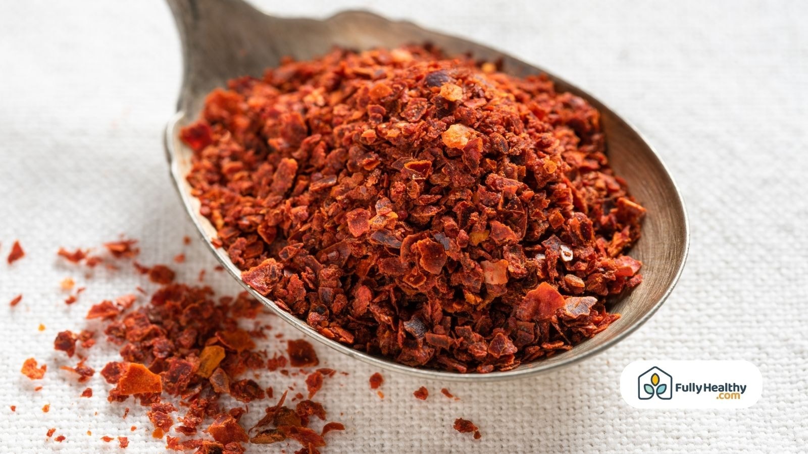 Spoonful of Aleppo pepper flakes with scattered crushed chiles on white cloth background